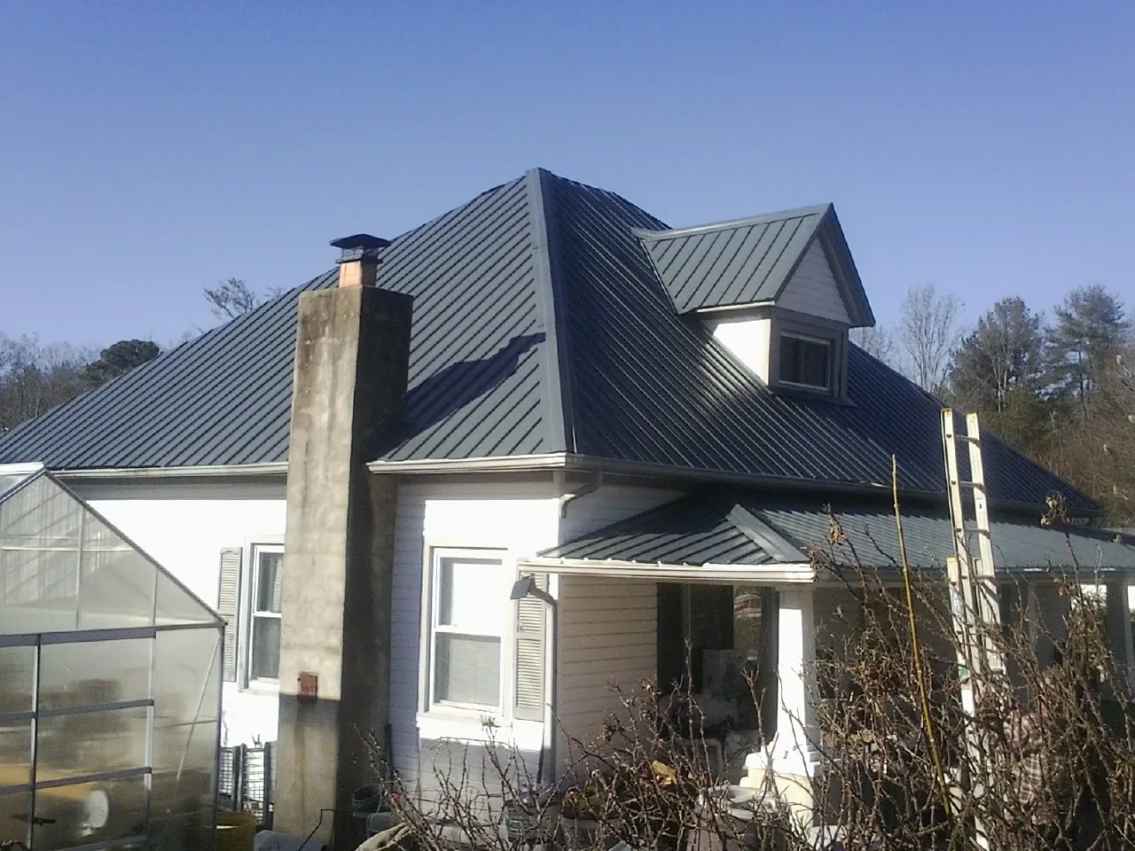 Dark blue standing seam metal roof on a white farmhouse with dormer — Slate & Tile Roof Repair by Roofing Brothers in Schellsburg