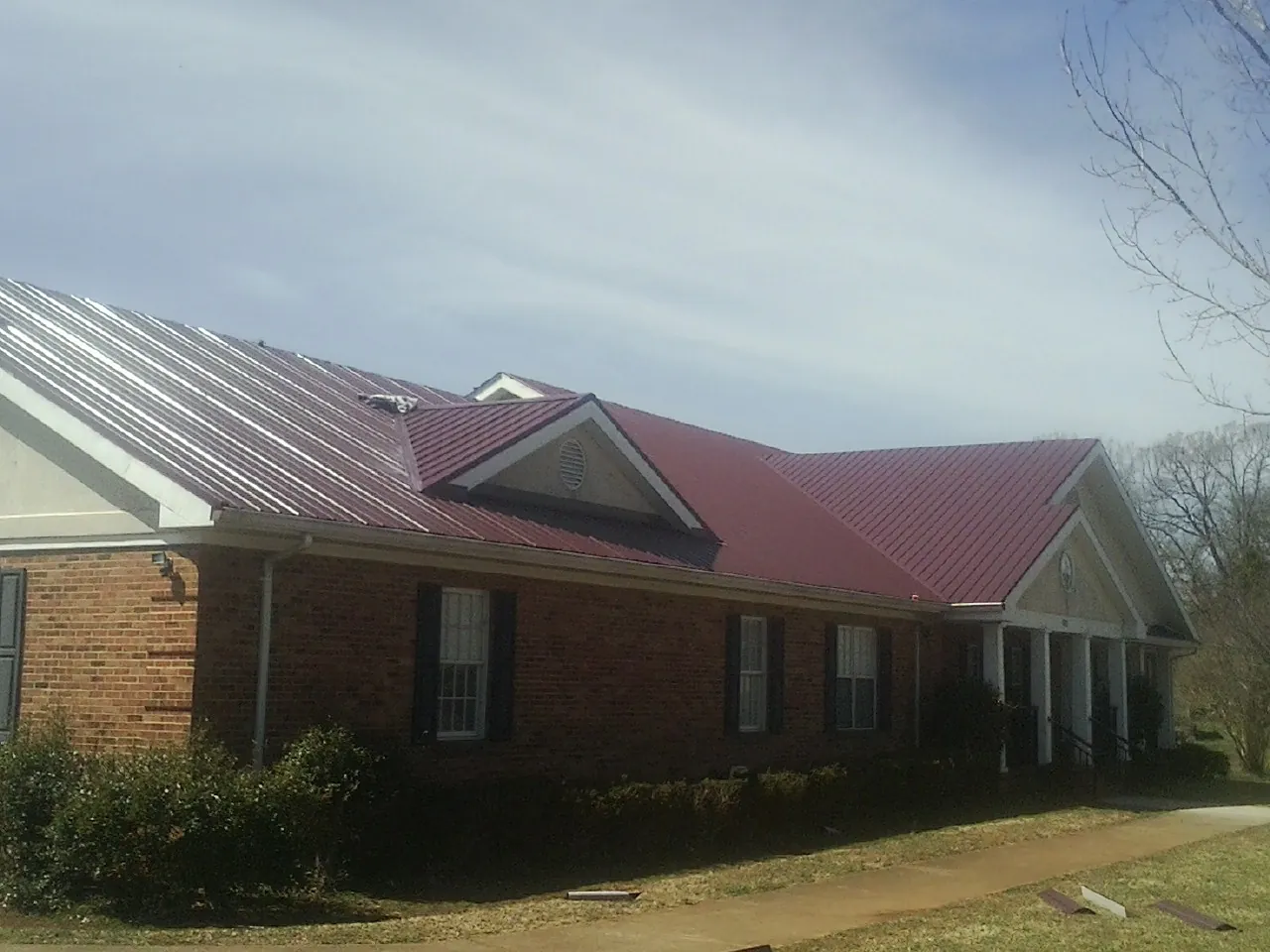Red metal roof with gabled entries on a long brick building, from a Hail Damage Roof Repair job in Schellsburg