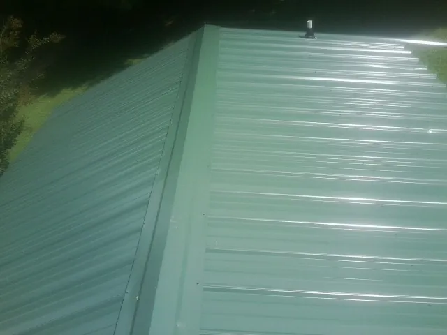 New green metal panels meeting at the ridge of a roof — Flat Roof Repair work by our crew in Schellsburg
