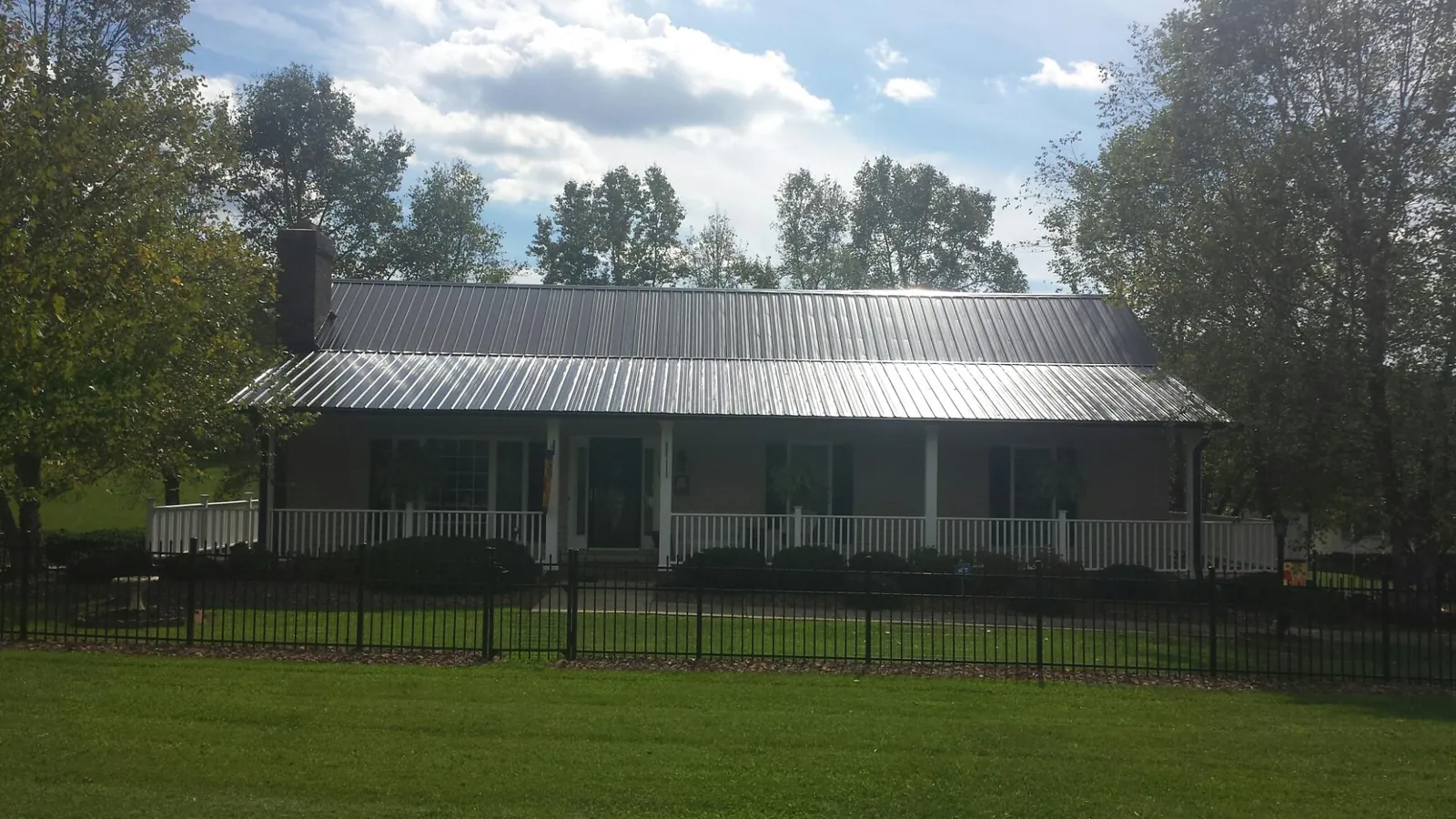 Gray metal roof on a brick ranch with a full width front porch — Gutter Guard Installation work by our crew in Schellsburg