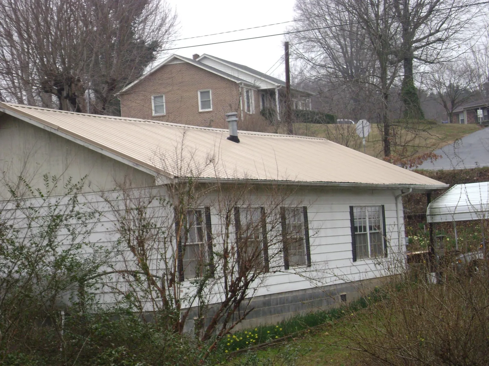 Tan metal roof on a white sided house set into a hillside — Commercial Roofing by Roofing Brothers in Schellsburg